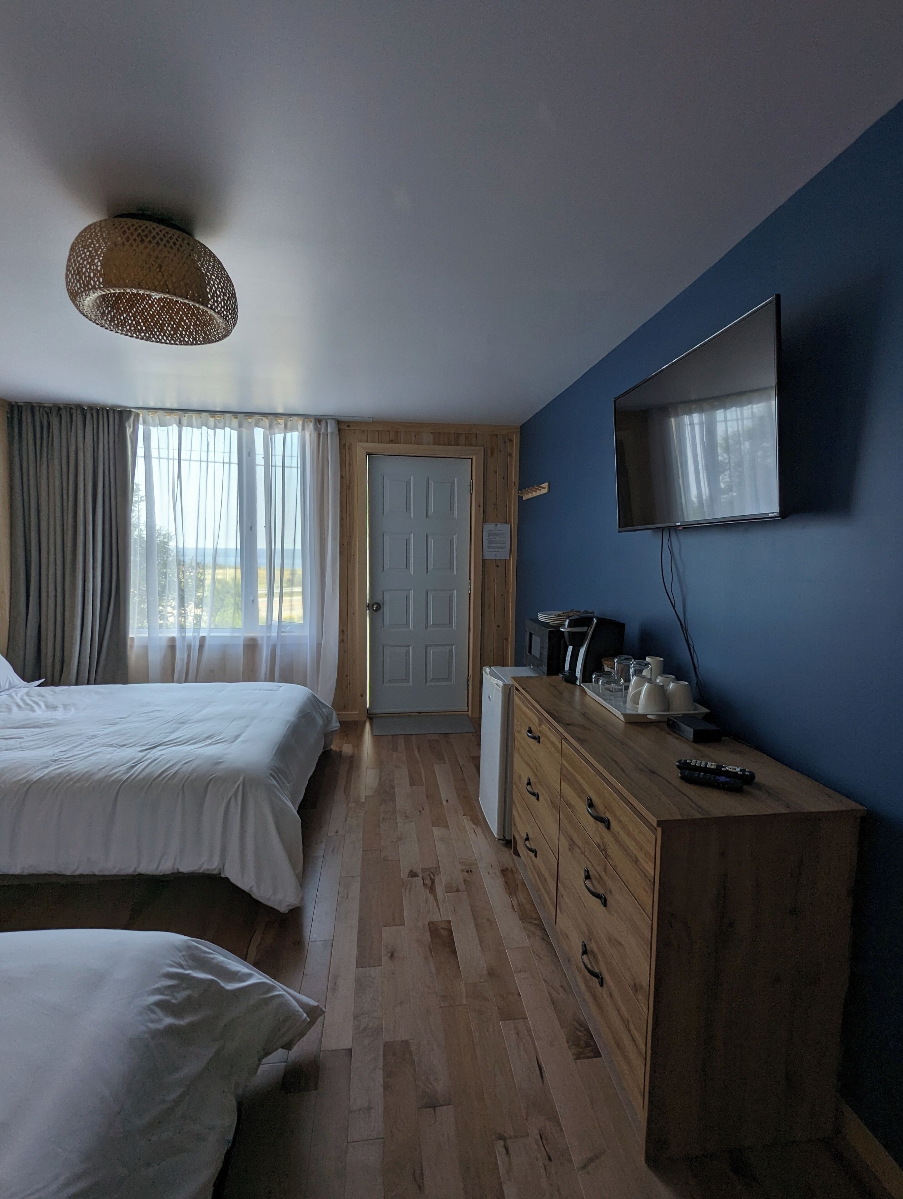 Un dormitorio con dos camas, un aparador de madera, un televisor y una puerta que da a un balcón.