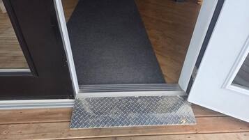 A wooden floor with a gray carpet leading to a door with a metal threshold.