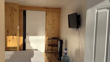 Ein Zimmer mit einem Bett, einem Sessel, einem Wasserspender, einem Fernseher und Holzwänden.