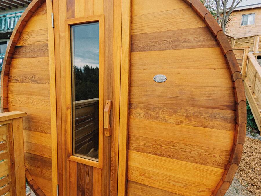 Una sauna de madera con puerta de vidrio, terraza de madera y placa de metal.