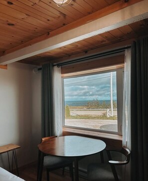 A room with a wooden ceiling, a table with two chairs, and a window with curtains.