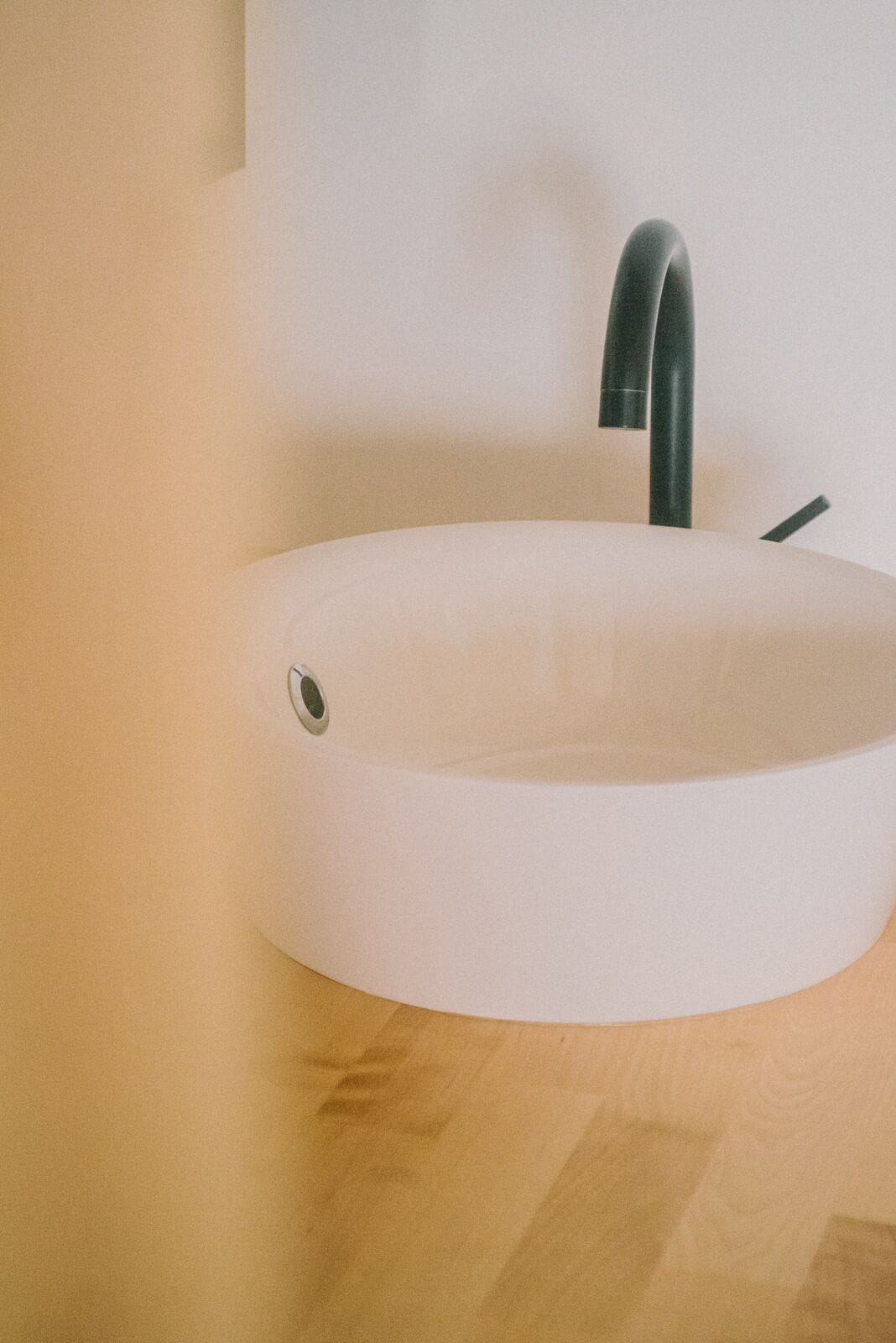 Ein modernes, rundes, weißes Waschbecken mit einem eleganten, schwarzen Wasserhahn auf einer Holz Arbeitsplatte.