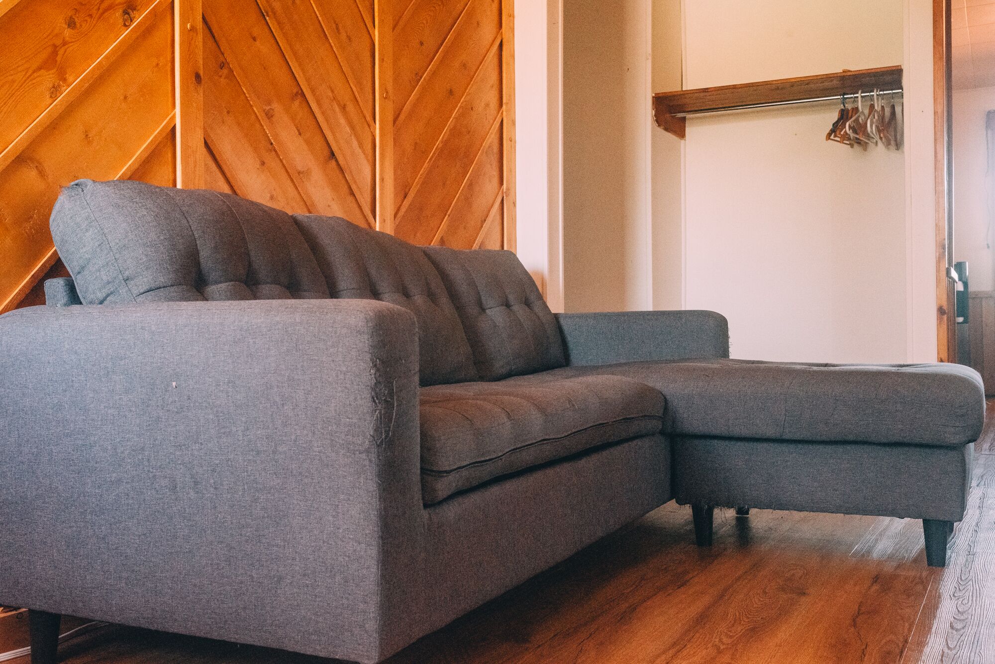 A gray sectional sofa in a room with wooden walls and a wooden floor.