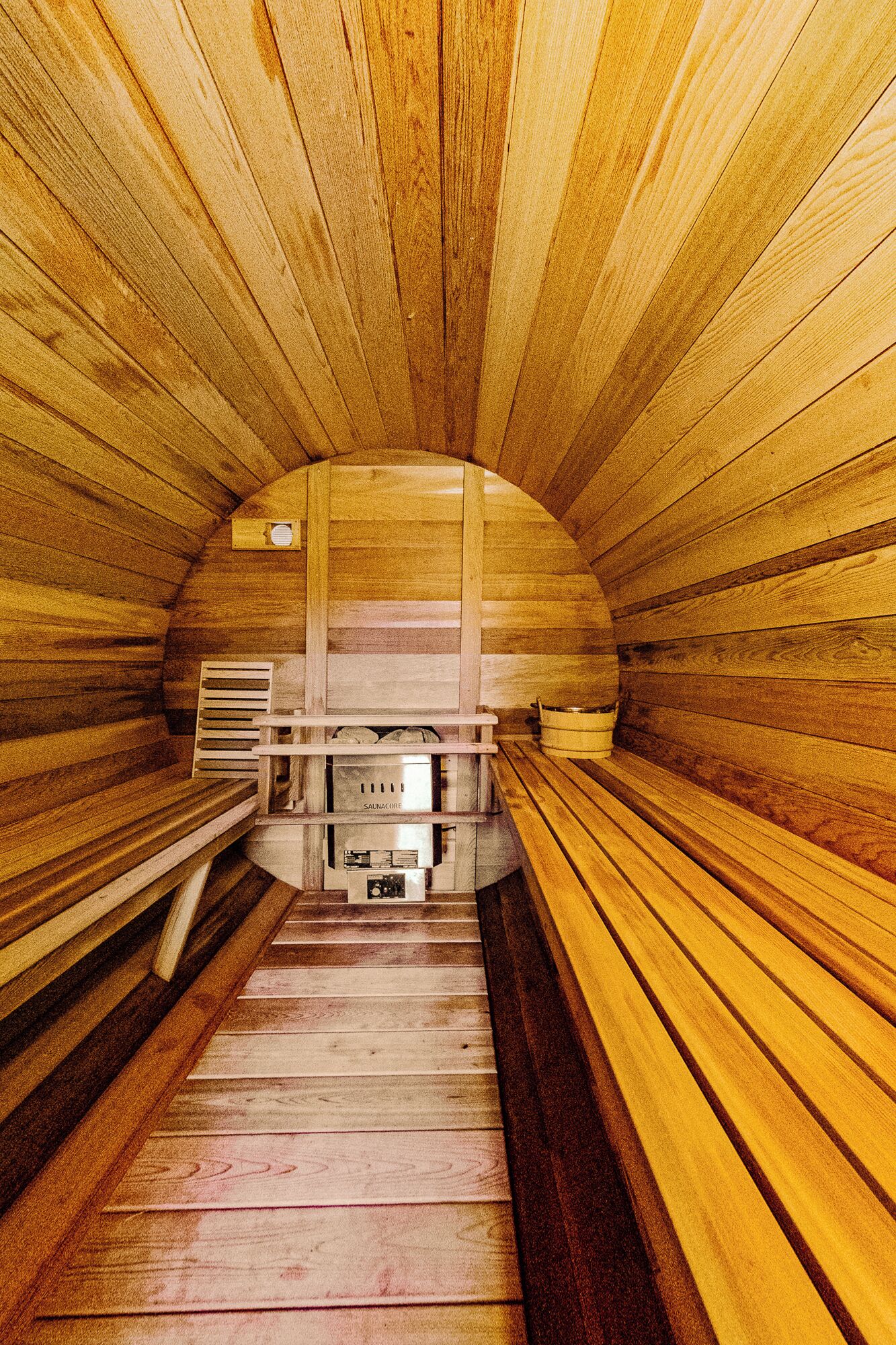A sauna with wooden walls and benches, a central heating unit, and a bench with a towel.