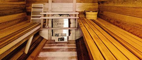 A sauna with wooden walls and benches, a central heating unit, and a bench with a towel.