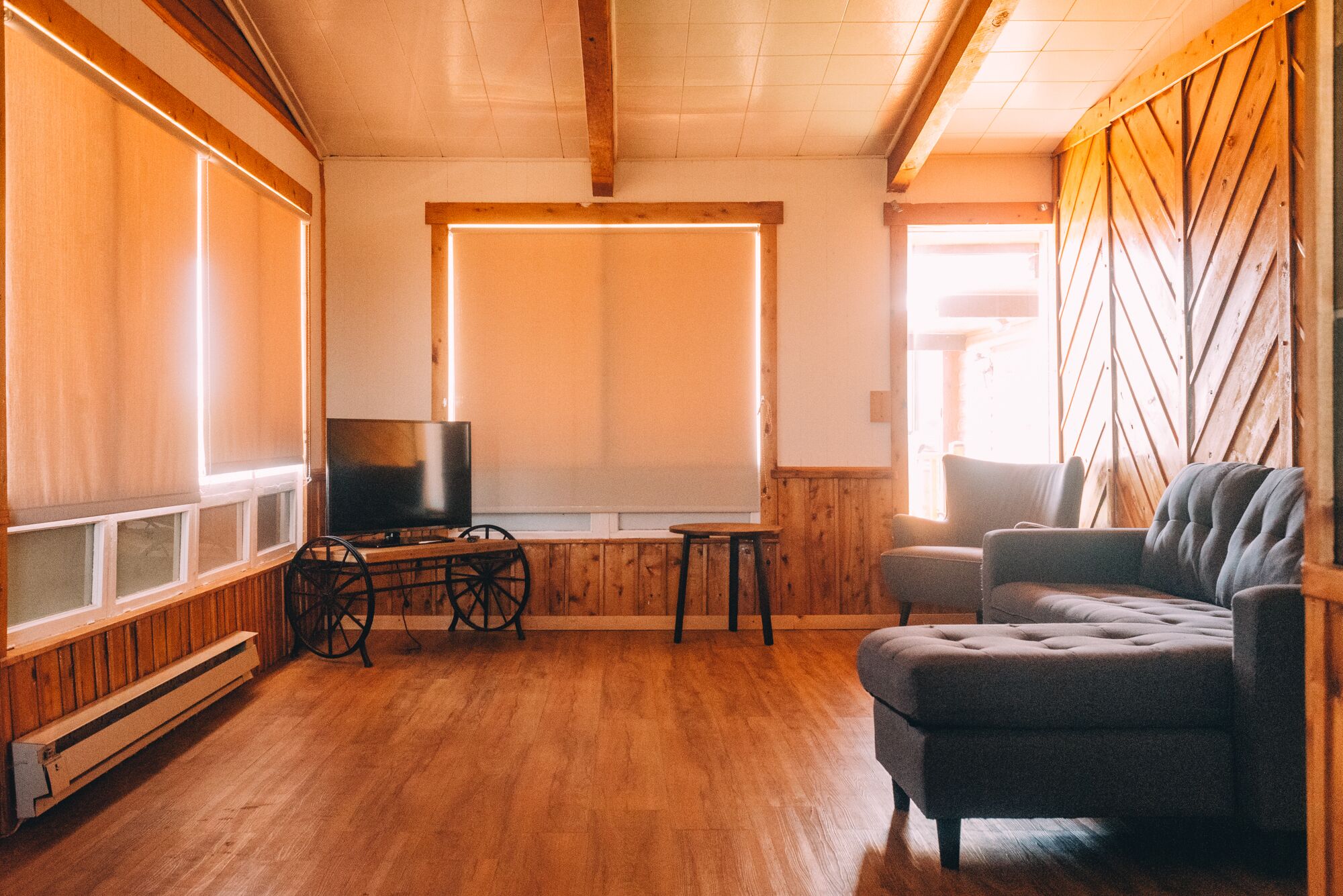 A cozy room with wooden walls and floors, a television on a wooden stand, a cushioned armchair, and a small table.