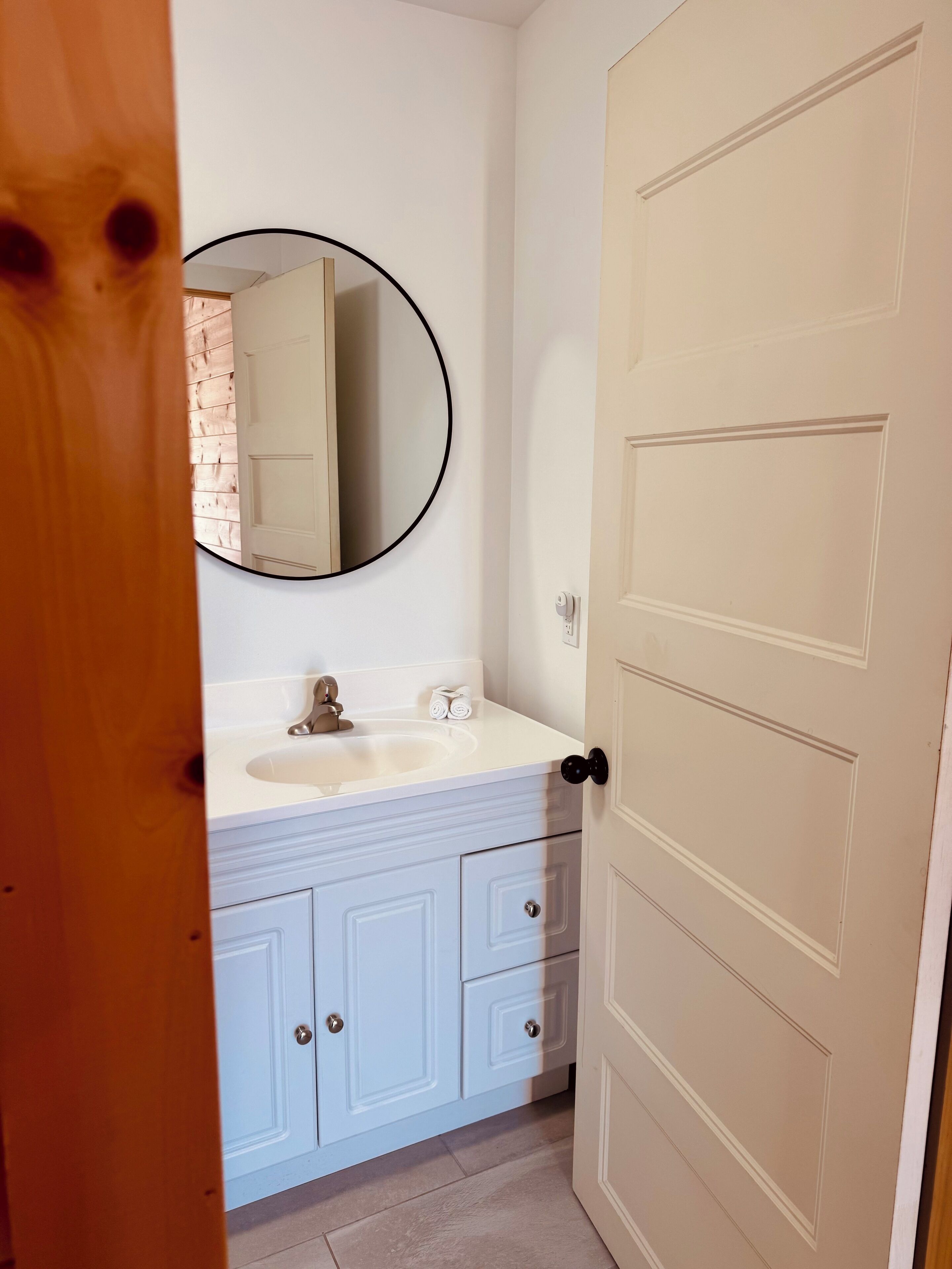A bathroom with a white sink, a round mirror, and light blue cabinets.