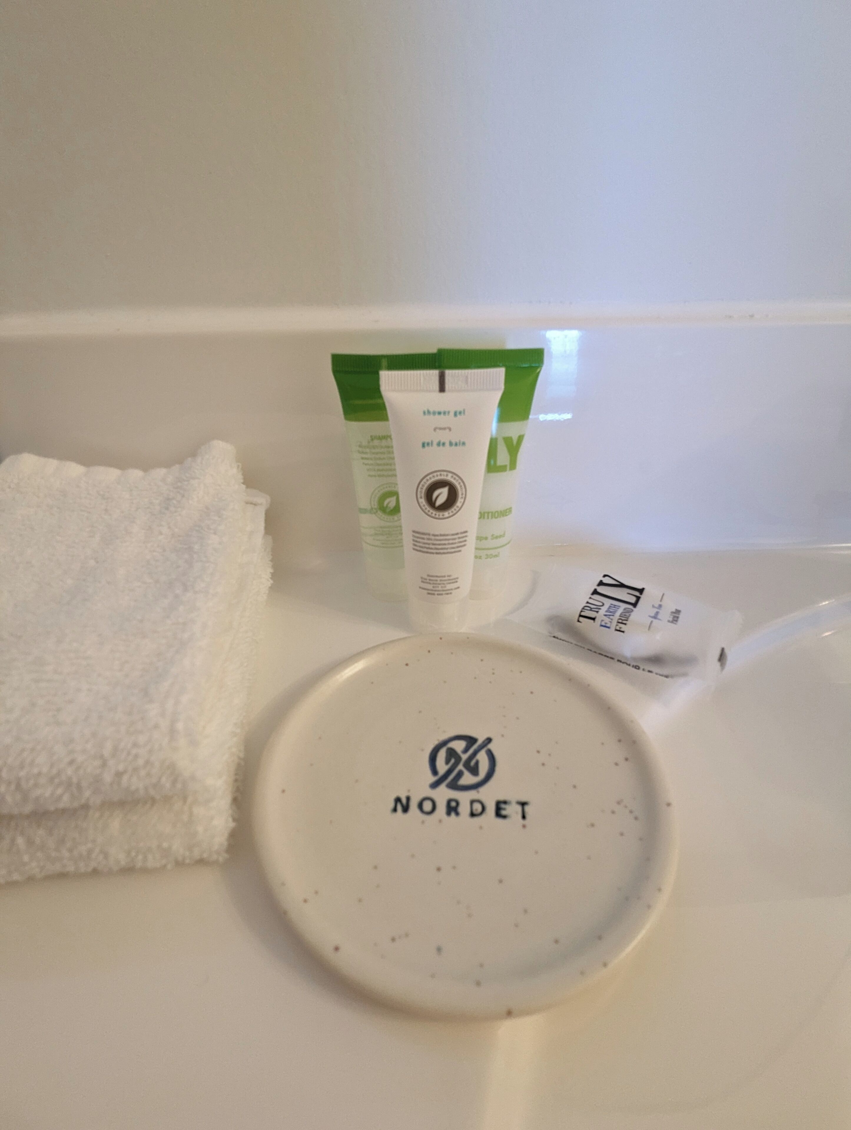 Un lavamanos con un jabonera de la marca Nordet, una toalla blanca y un tubo de gel de ducha Nordet.
