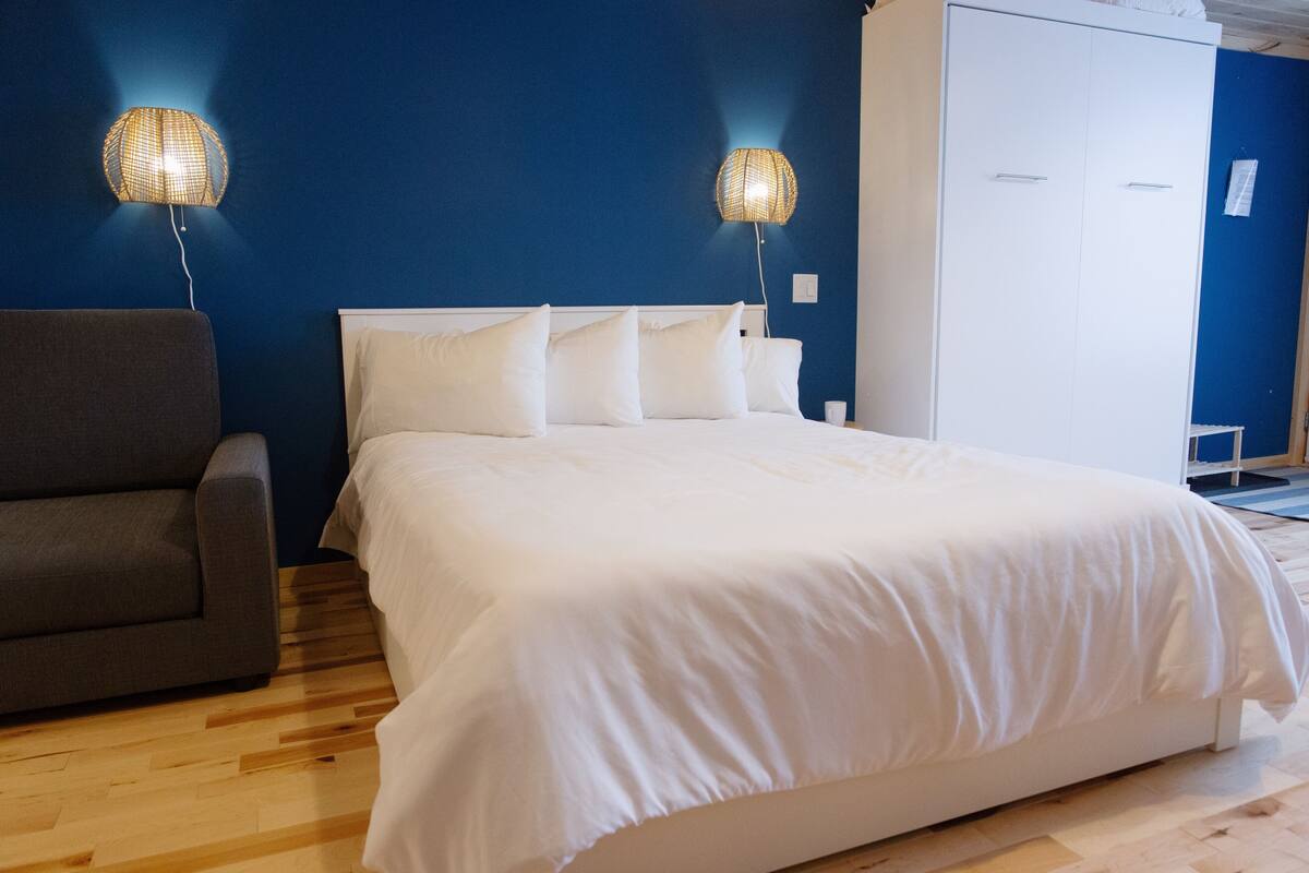 A bedroom with a bed, a grey armchair, and two wall-mounted lamps.