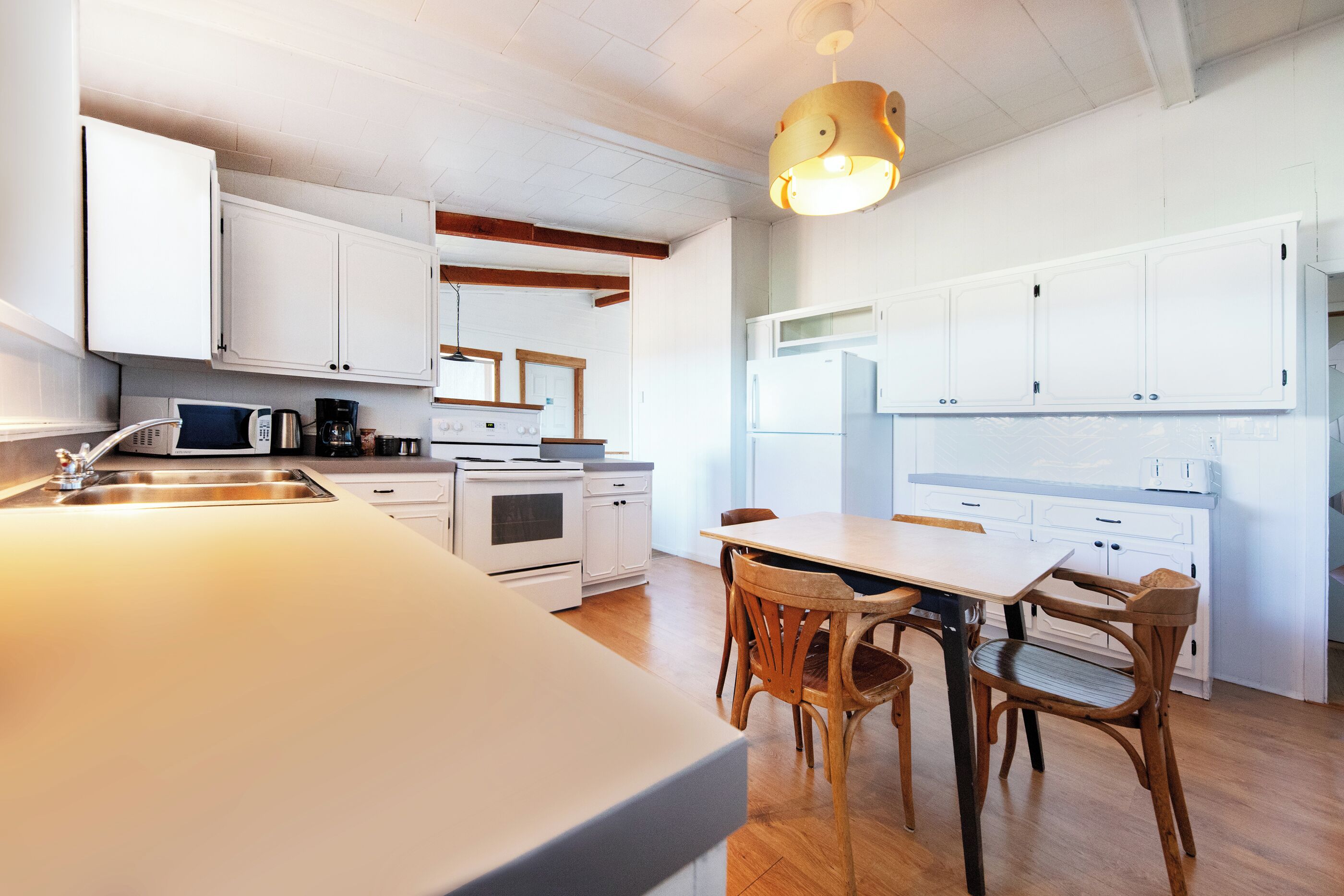 Een moderne keuken met witte kasten, een houten eettafel en een hanglamp.