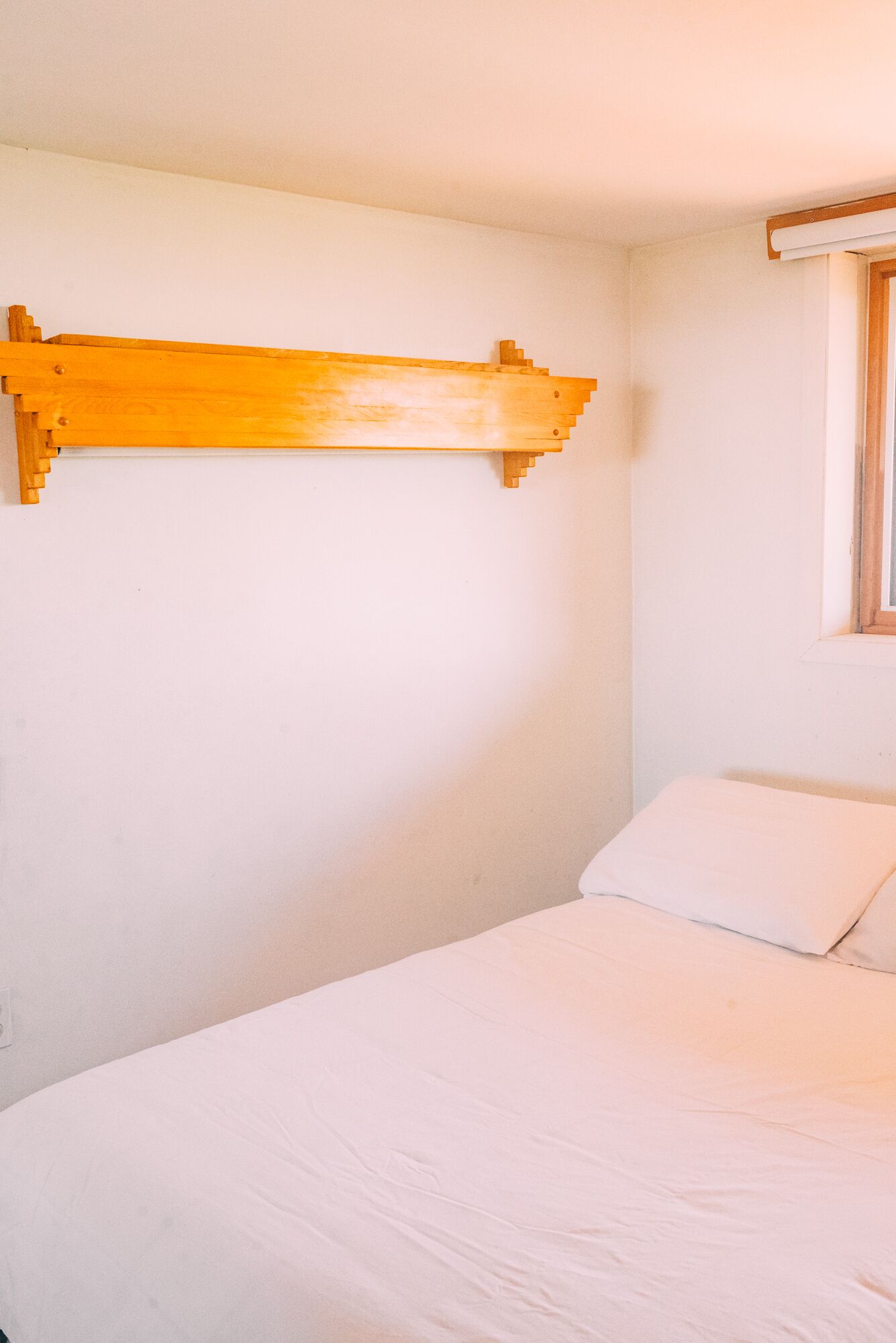 Une pièce simple, avec un lit, une tête de lit en bois et une fenêtre.