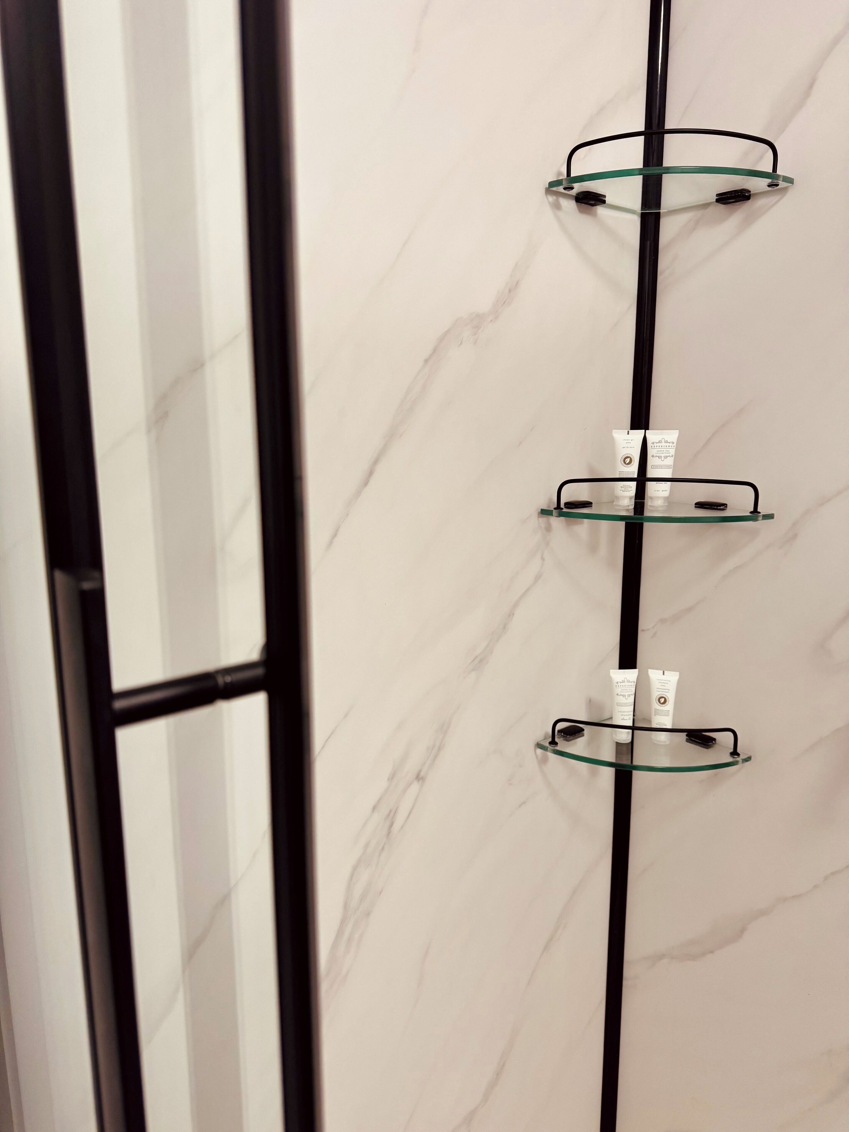 Un baño con pared de mármol, tres estantes de cristal y una barra vertical negra.