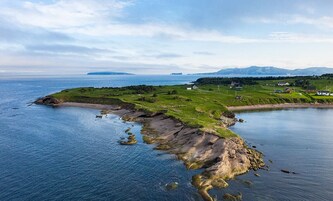A coastal landscape with a small island, rocky shoreline, and a distant mountain range.