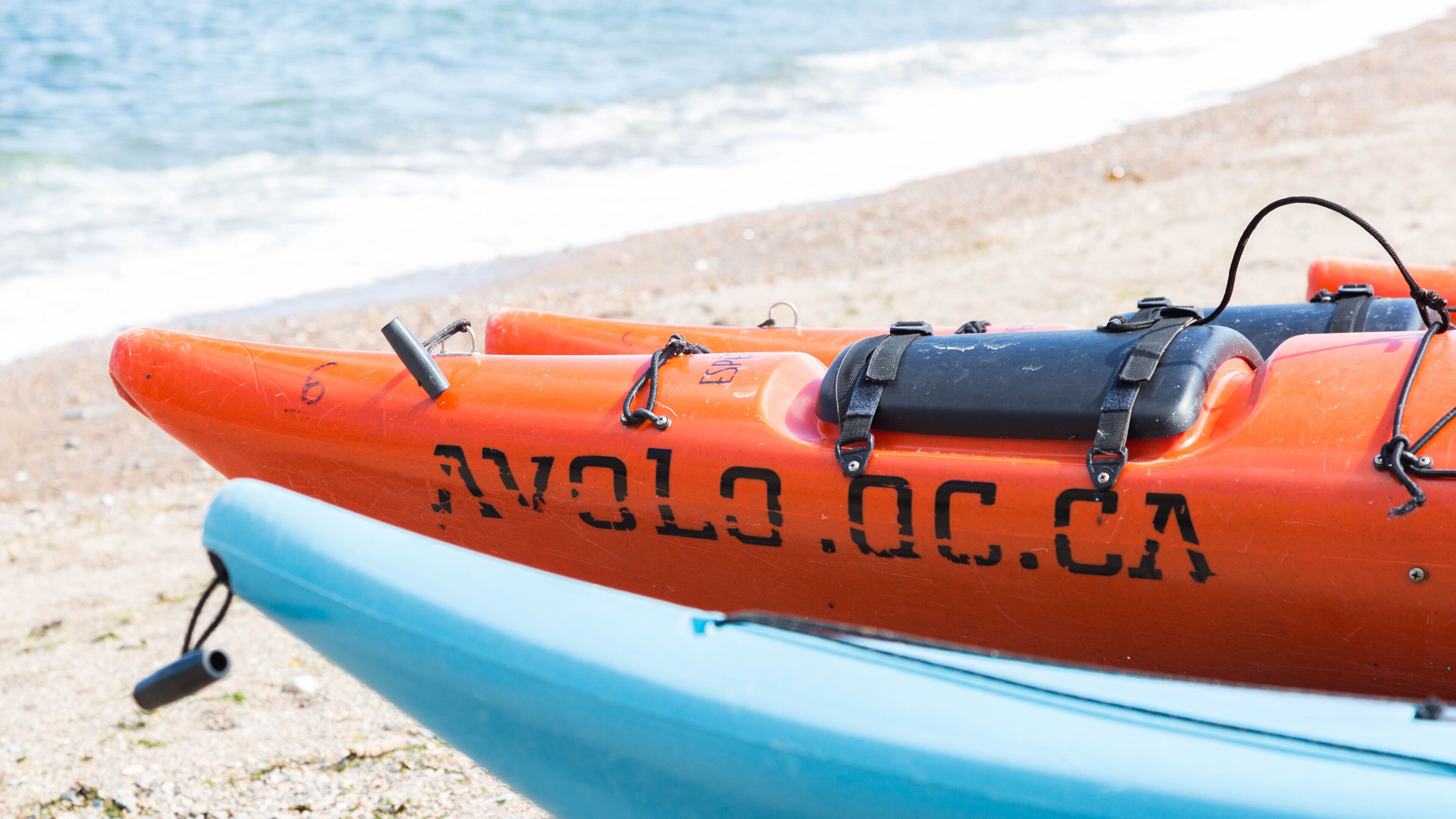 A lifeboat with the text "AVOLO.OC.CA" on it, placed on a sandy beach.
