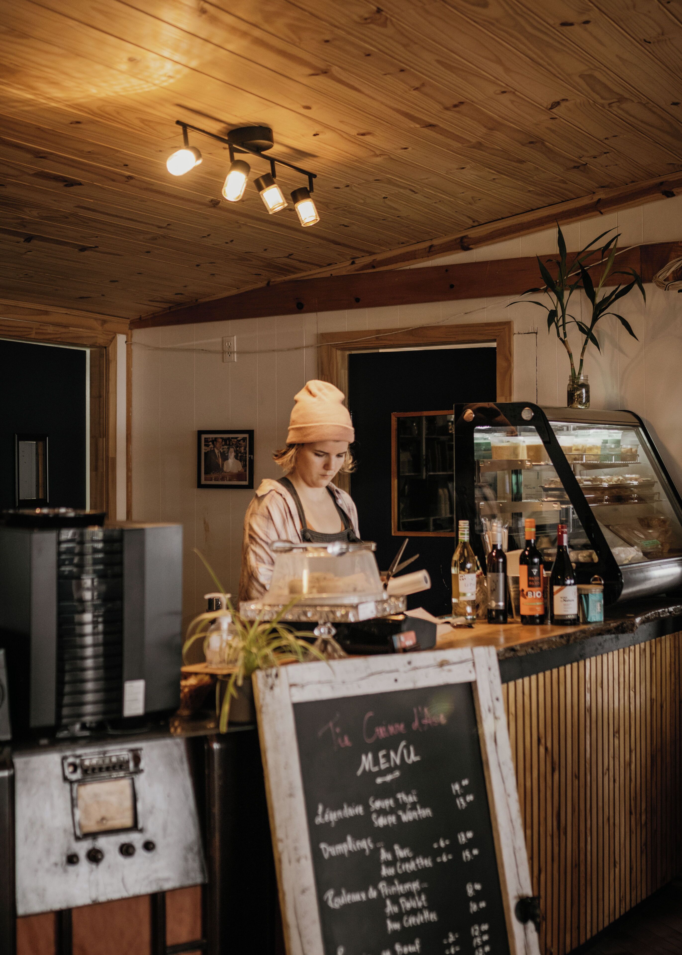 A restaurant interior with a wooden ceiling, a chalkboard menu, and a counter with a display case.