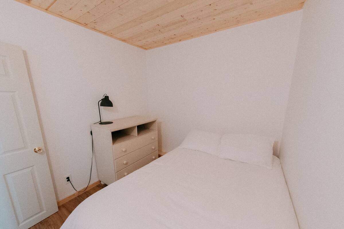 A bedroom with a bed, a dresser, a desk with a lamp, and a door.