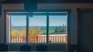 A room with a large window offering a view of the sea and greenery.