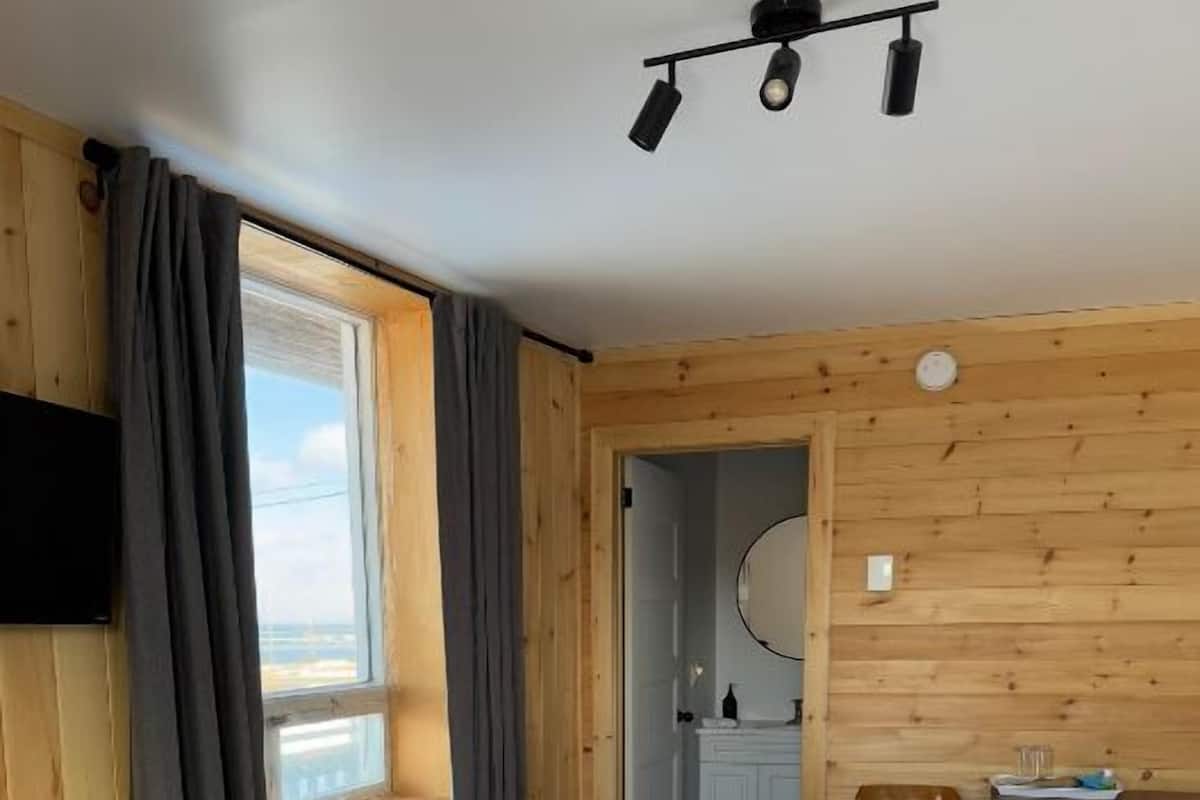 A wooden-paneled room with a bed, a desk, and a mirror.