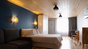 A bedroom with a bed, a sofa, two wall-mounted lamps, a wooden ceiling, and a desk with a chair.