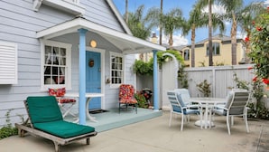 Une terrasse couverte avec une porte bleue, un fauteuil de jardin vert et une table avec des chaises.