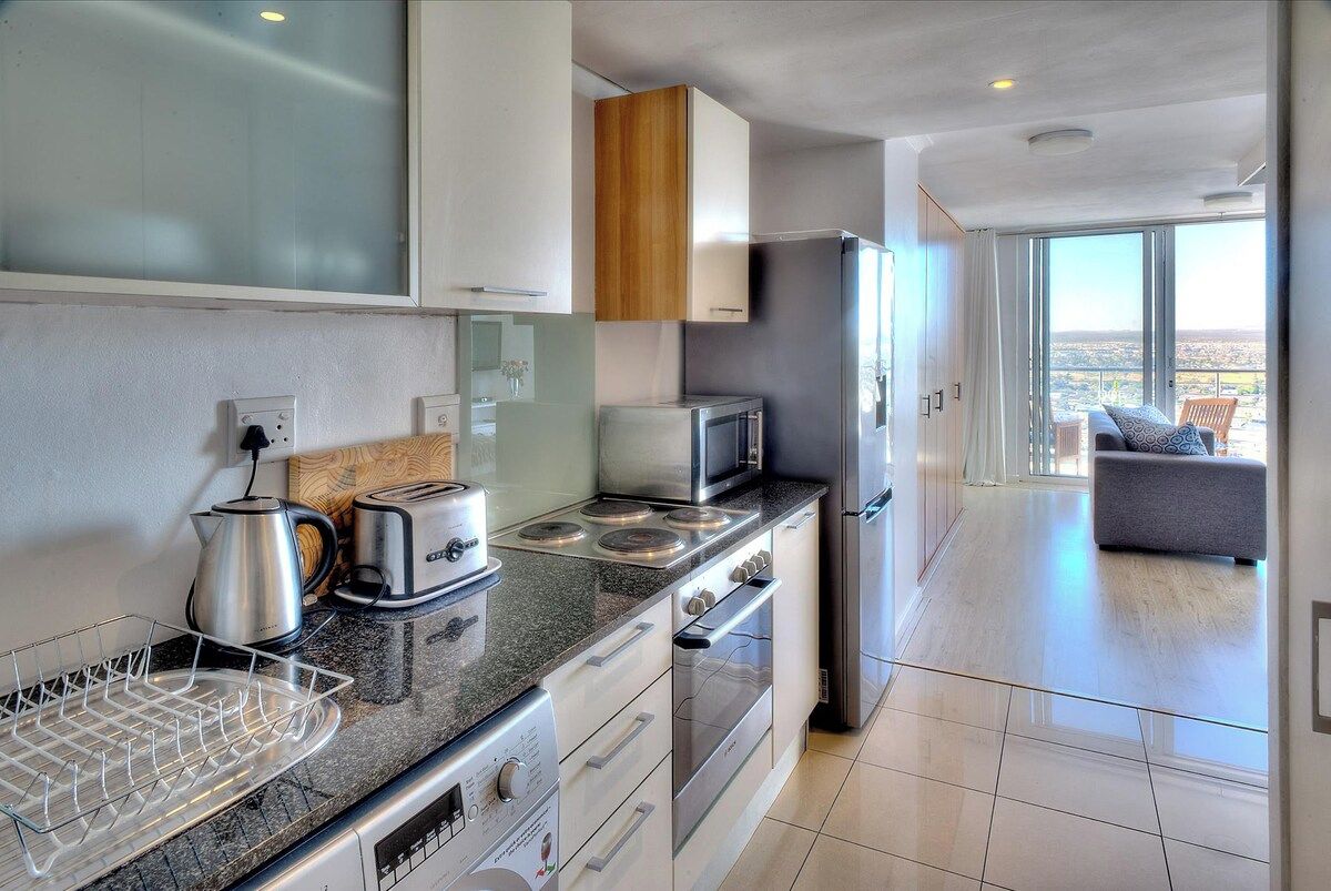 A modern kitchen with stainless steel appliances, a wooden cabinet, and a view to a balcony with a sofa.