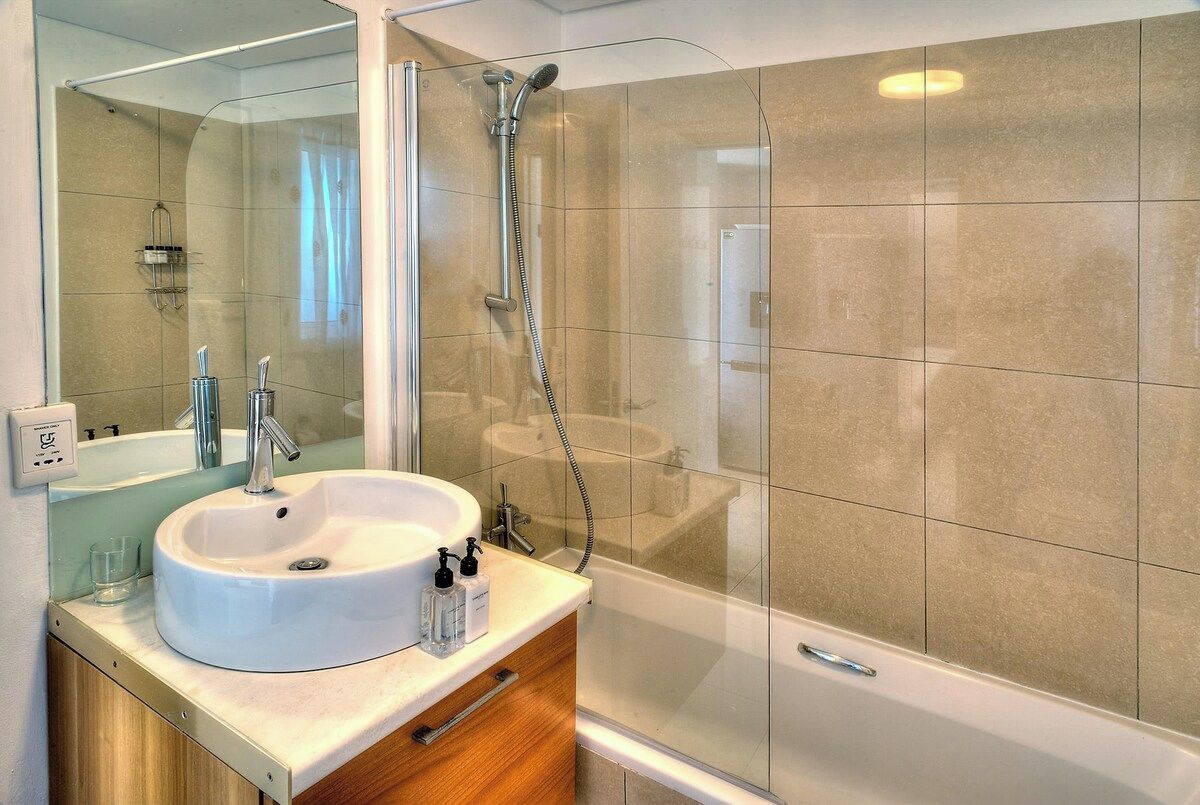 Een moderne badkamer met een douchecabine van glas, een wit wastafeltje en een houten badkamerkast.