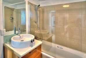 A modern bathroom with a glass-enclosed shower, a white sink, and a wooden vanity. - Cozy Beachfront apt | Sea views Balcony Pool (Bloubergstrand)