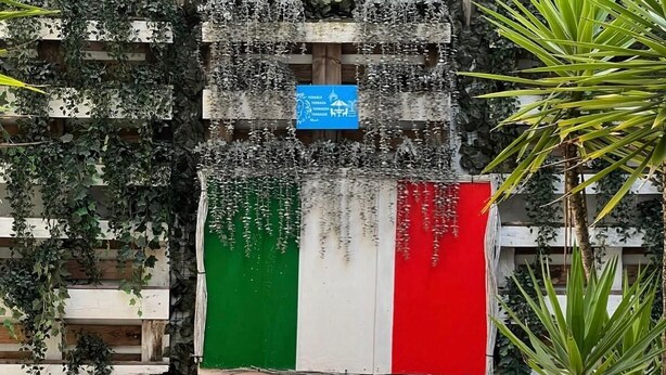 A wooden outdoor seating area with a chair and table, surrounded by a wall decorated with greenery and a flag. - Lion University & Youth Hostel Milano (Milan)