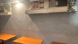 A room with two wooden tables and chairs, a shelf with plants and a poster, and a wall-mounted light fixture. - Lion University & Youth Hostel Milano (Milan)