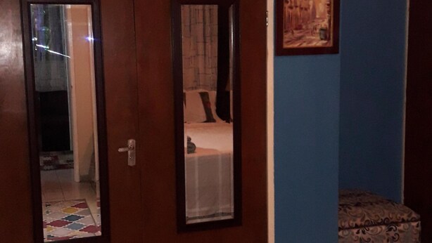 A bedroom with a bed, a wardrobe, a mirror, a painting, and a patterned rug. - Just Like Home, New Kingston (New Kingston)