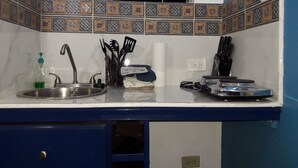 A kitchen with a sink, faucet, and various utensils. There is a window with blinds above the sink. - Just Like Home, New Kingston (New Kingston)