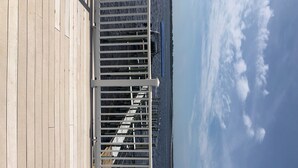 A wooden deck with a white railing overlooking a body of water and a distant landmass. - Bayfront Condo with Boat Slip (Panacea)