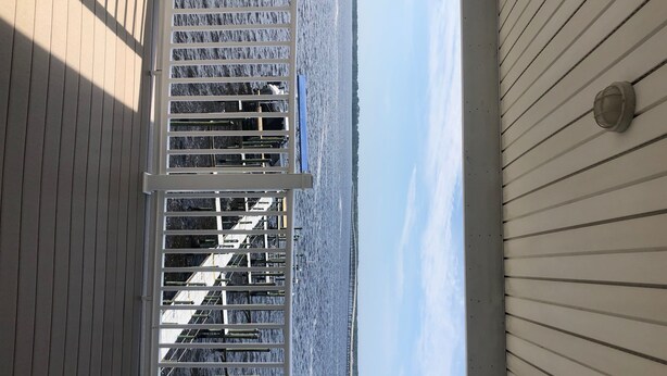 A view through a window with a metal railing, overlooking a body of water and a distant shoreline. - Bayfront Condo with Boat Slip (Panacea)