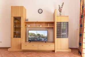 Un salon avec un téléviseur, des meubles en bois, une horloge et un vase rempli de fleurs.