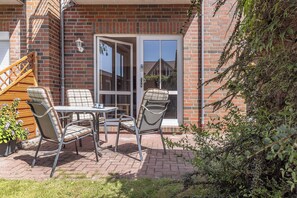 A patio with a table and chairs, a wooden staircase, and a brick wall. - This bright holiday home on the ground floor offers on its approx. (Carolinensiel)