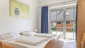 A bedroom with a bed, a bedside lamp, a window with a view of a building, and a painting on the wall. - This bright holiday home on the ground floor offers on its approx. (Carolinensiel)