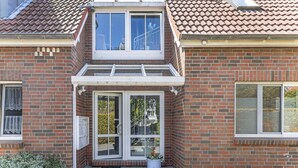 A two-story house with a brick exterior, a front porch, and a small garden area. - This bright holiday home on the ground floor offers on its approx. (Carolinensiel)