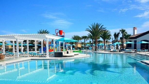 A pool area with lounge chairs and umbrellas, a water slide, and a covered seating area. - Luxurious Vacation Townhome With Private Pool (Kissimmee)