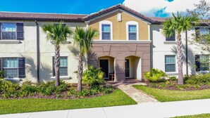A two-story residential building with a symmetrical facade, a central entrance with an archway, and a tiled roof. - Luxurious Vacation Townhome With Private Pool (Kissimmee)