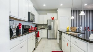 A modern kitchen with white cabinets, stainless steel appliances, and a red rug. - Luxurious Vacation Townhome With Private Pool (Kissimmee)