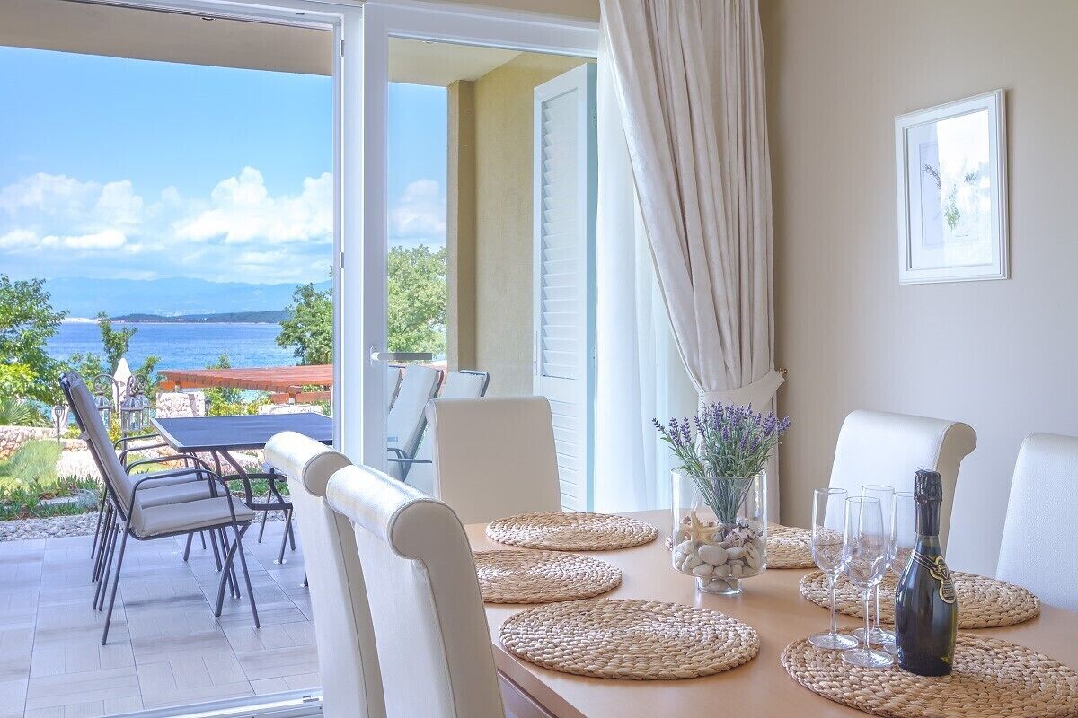 Un comedor con una mesa preparada para cuatro personas, con vistas a un paisaje marino.