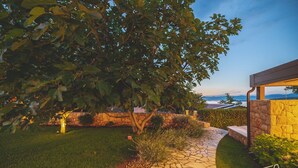 A stone pathway leading to a building with a stone wall and a view of the sea.