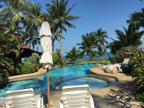 A pool area with lounge chairs, a white umbrella, and palm trees.