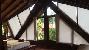 Een kamer met een schuine kap, een bed met matras en kussens, een houten bankje en een tafel.