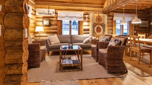 A cozy log cabin interior with a sofa, wicker chairs, a coffee table, and a dining table.