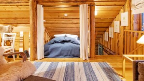 A cozy wooden cabin room with a bed, a chair, a small table, and a hanging light fixture.