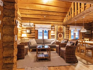 A cozy log cabin interior with a sofa, chairs, a coffee table, and a dining area.