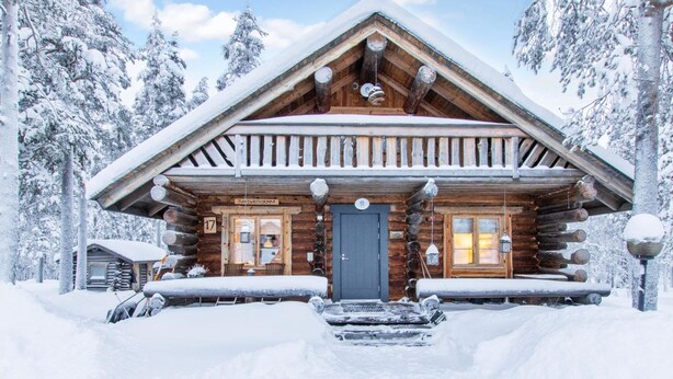 A log cabin with a dark entrance door, a wooden porch, and a sign above the door.