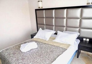 A neatly made bed with a floral-patterned bedspread, a headboard with a tufted design, and a bedside table with a lamp.