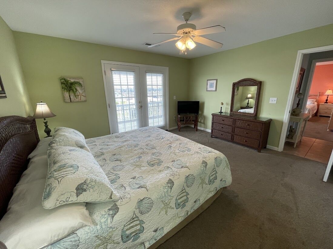 Une chambre à coucher comprenant un lit, une commode, un téléviseur et un ventilateur de plafond.